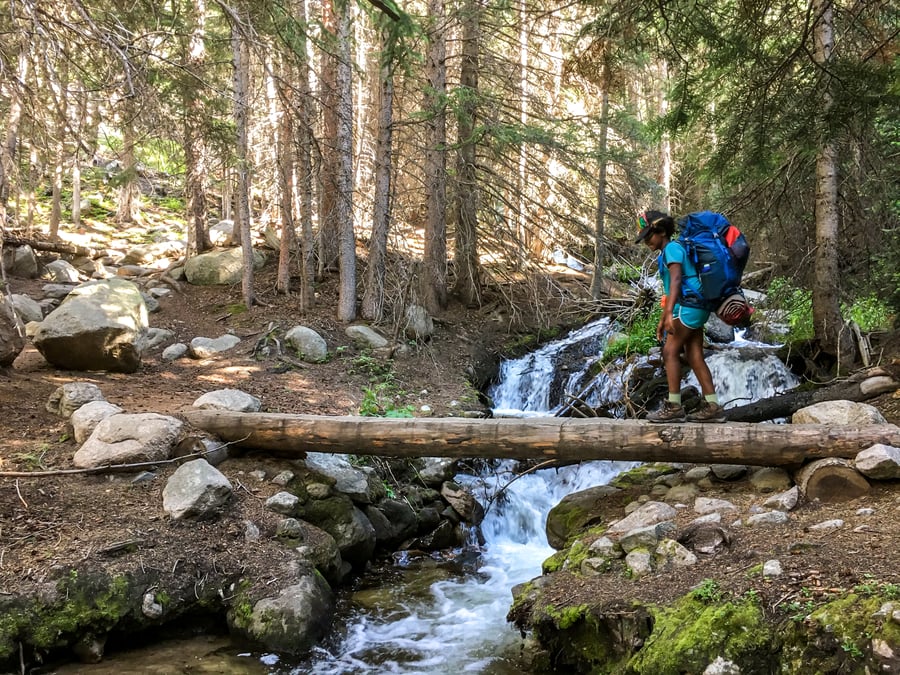 teen crossing a river while backpacking in the mountains