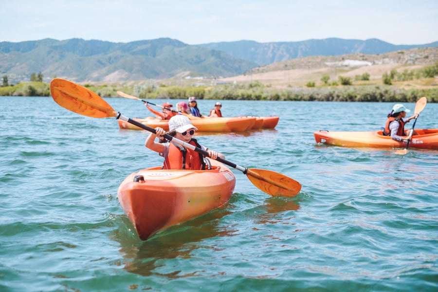 child kayaking in a lake with mountains in background