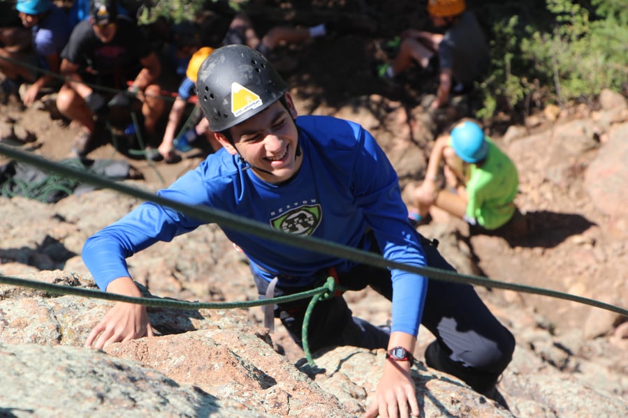 teen smiling while making it to the top of a climbing route outdoors